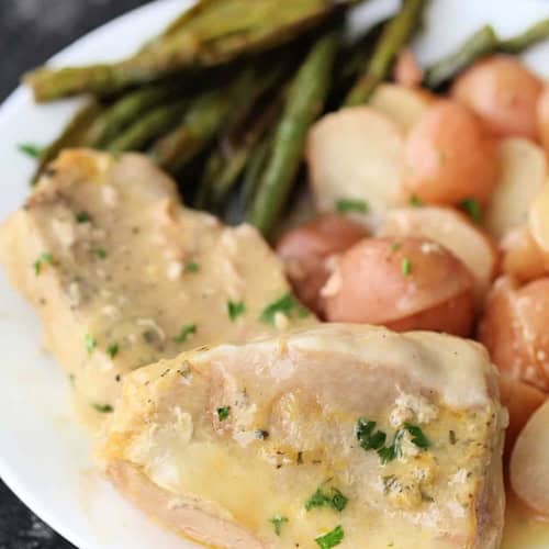 A white plate with two pieces of slow cooker pork, roasted green beans, and sliced red potatoes.