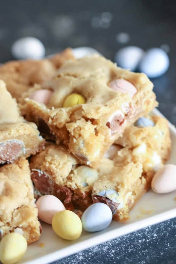 Cadbury Mini Egg Blondies sliced into squares on a plate surround by Cadbury Mini Eggs.