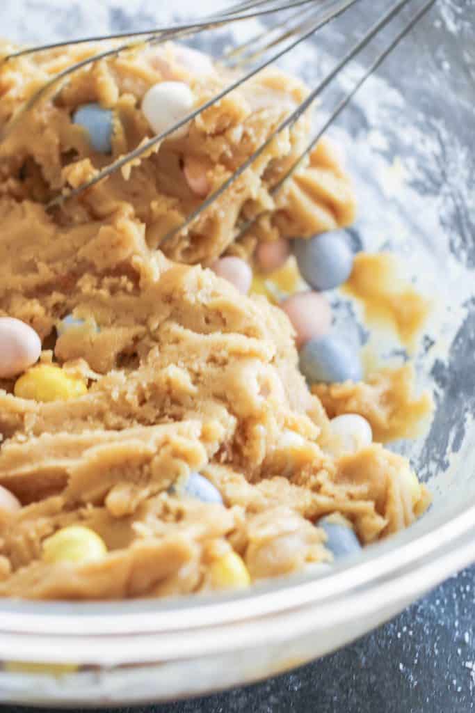Cadbury mini eggs added to dough in glass mixing bowl.