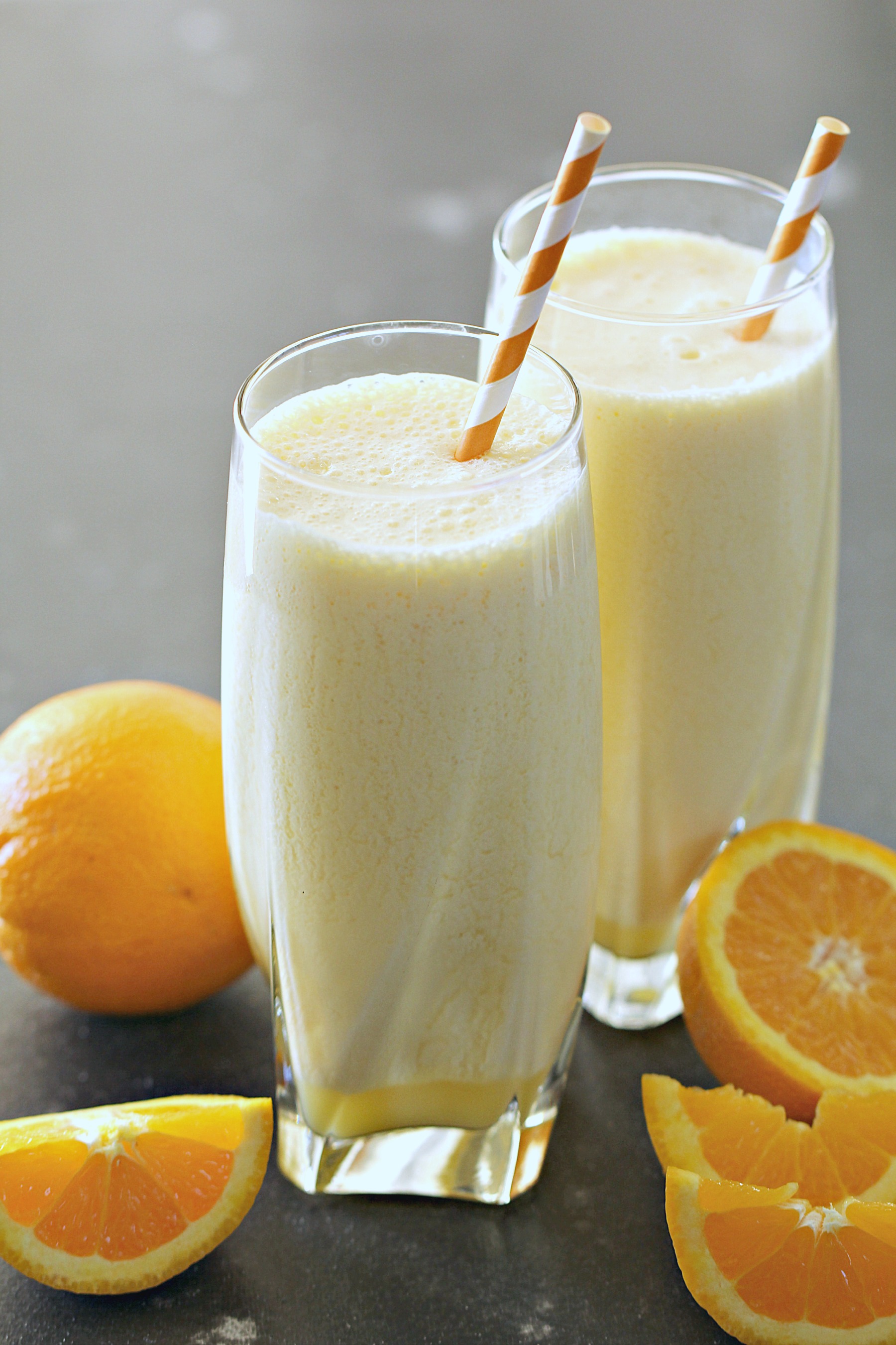 Two glasses of Orange Julius Copycat with Bananas surrounded by oranges
