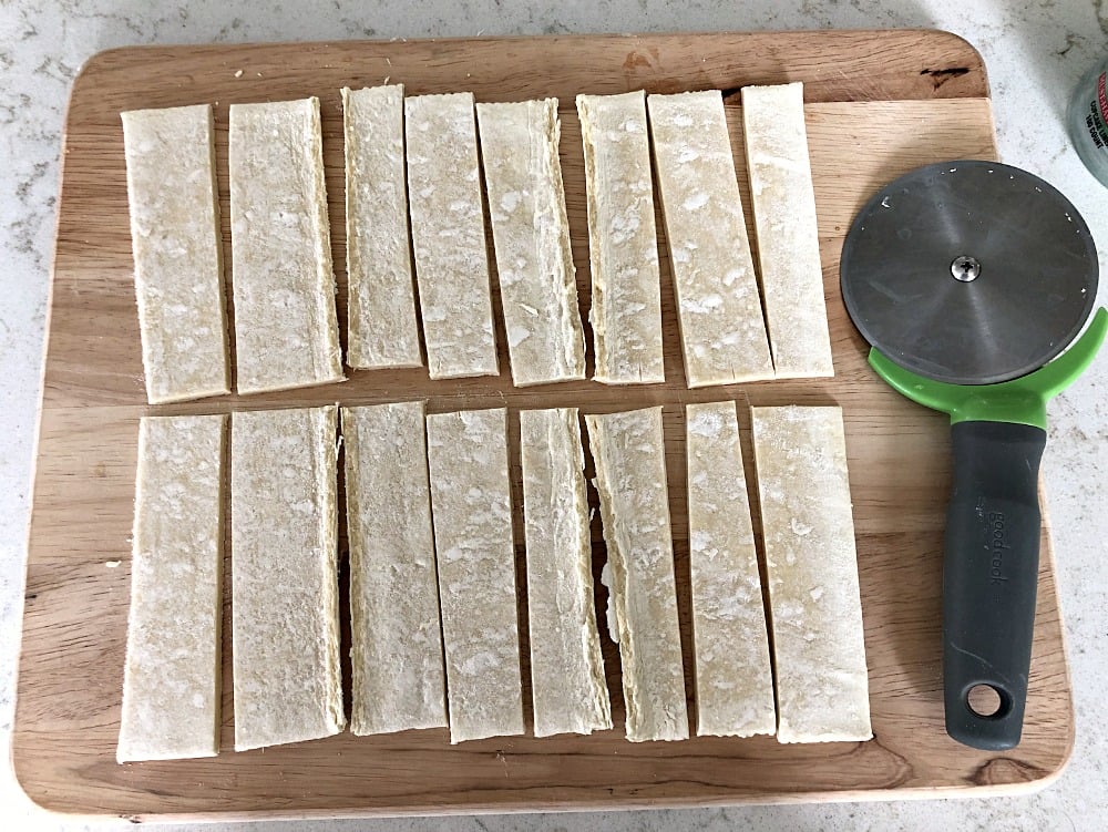 Puff pastry on a cutting board with a pizza cutter sliced into strips