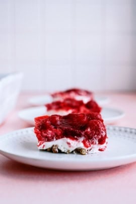 Close-up of a dessert plate featuring a square slice of layered strawberry pretzel salad with a pretzel crust, cream cheese center, and strawberry gelatin topping.