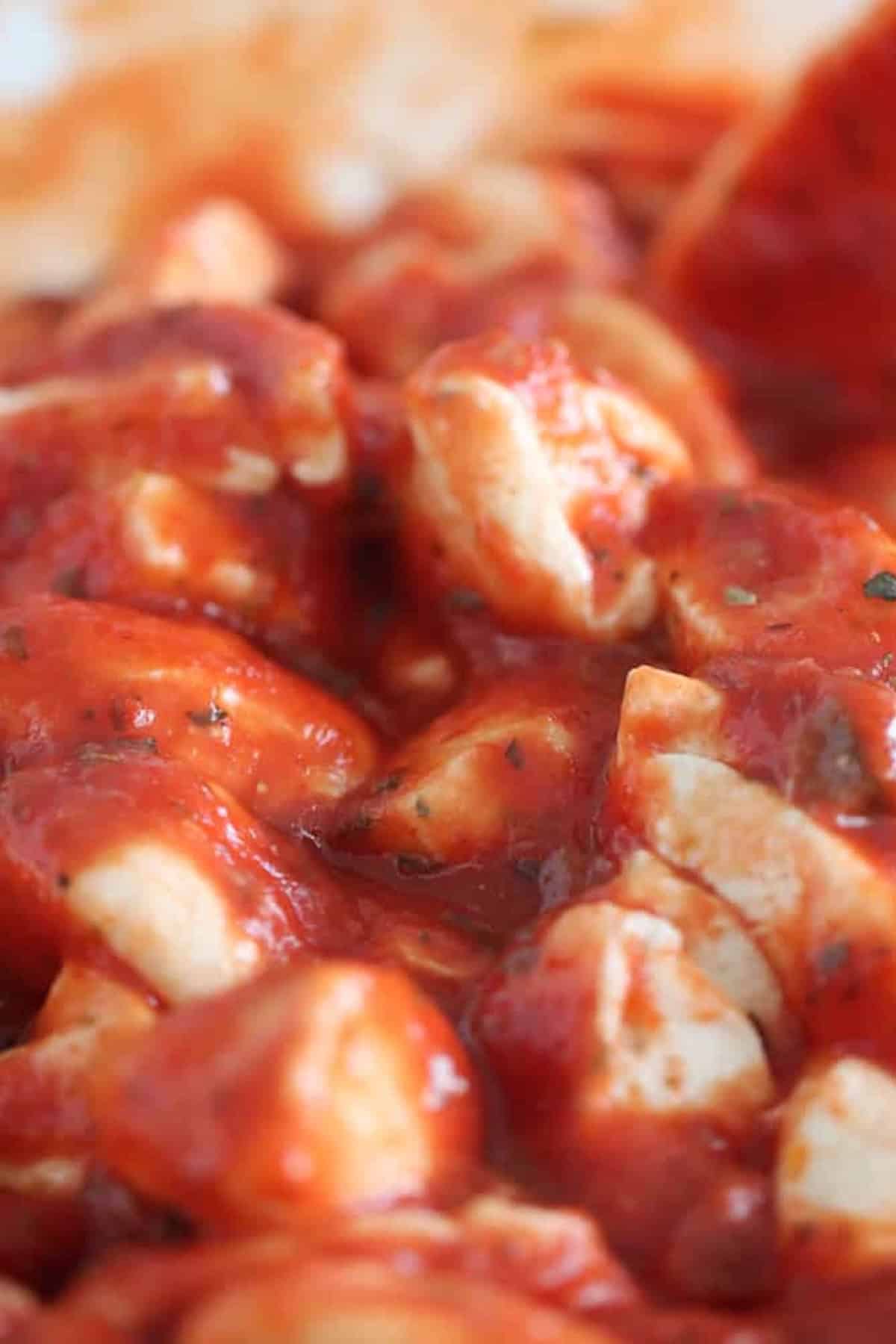 Close-up of diced chicken pieces covered in red tomato sauce with visible herbs.