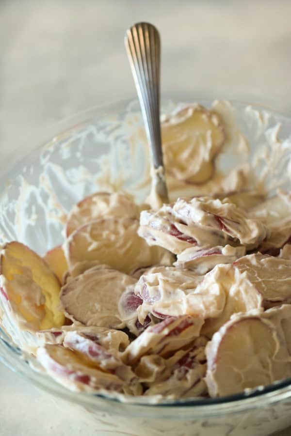 Mixing potatoes with sour cream mixture in a glass bowl