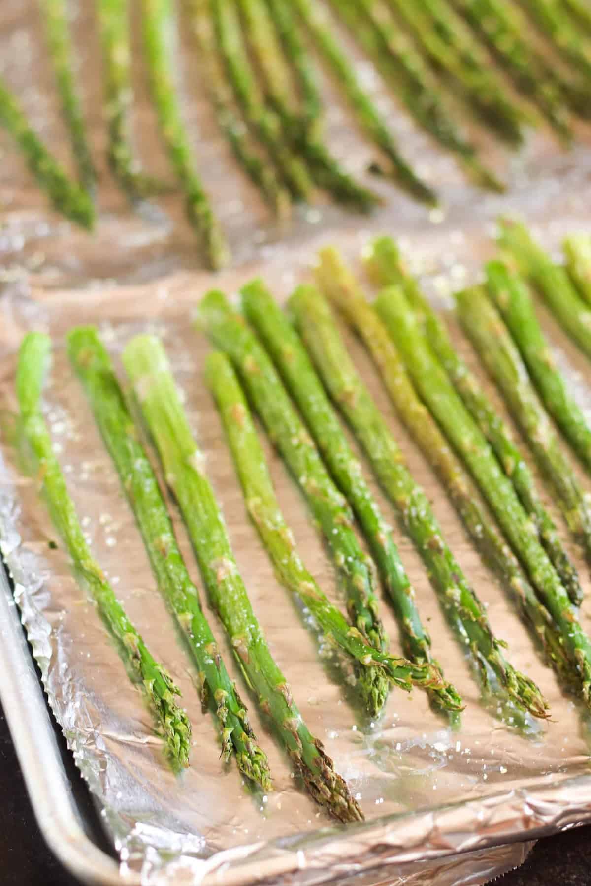 Roasted asparagus spears arranged on a foil-lined baking sheet, lightly sprinkled with salt.