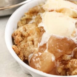 A close-up of apple cobbler topped with a scoop of vanilla ice cream in a white bowl.