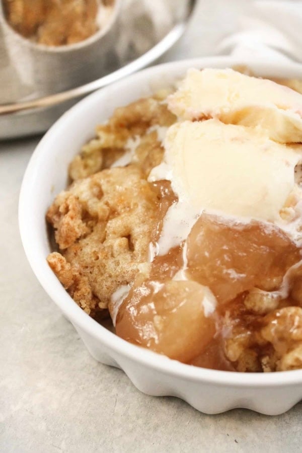 A close-up of apple cobbler topped with a scoop of vanilla ice cream in a white bowl.