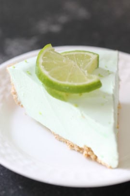 Slice of Key Lime Pie on a white plate topped with 2 slices of fresh lime.