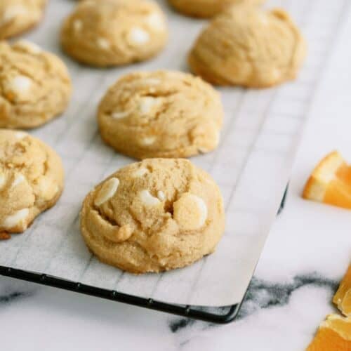 Orange Creamsicle Cookies on a lined cooling rack with sliced oranges off to the sides.