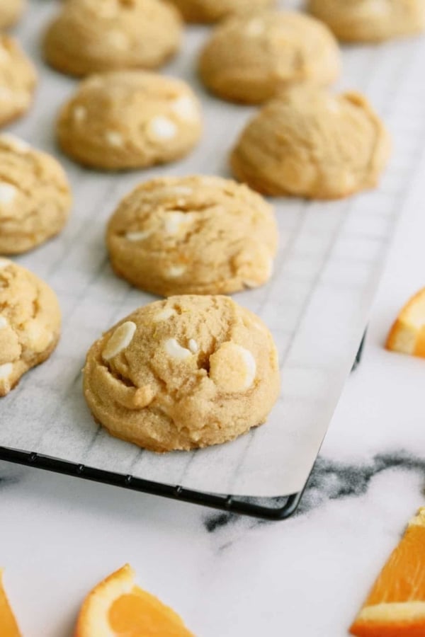 Orange Creamsicle Cookies on a lined cooling rack with sliced oranges off to the sides.