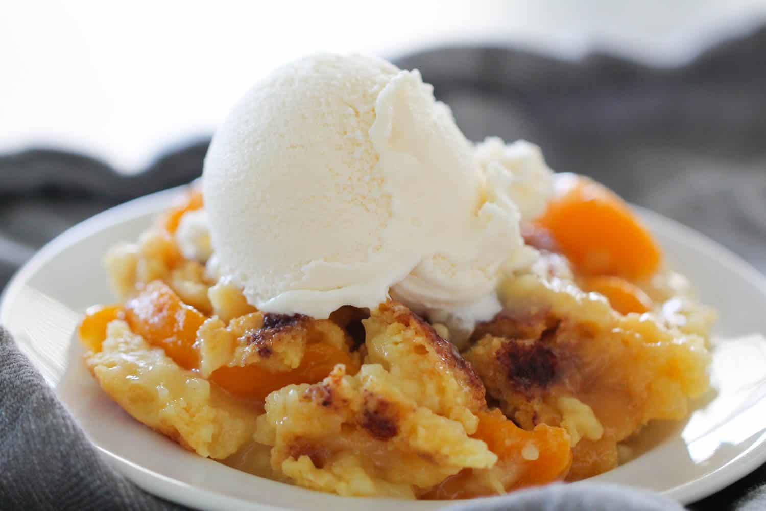 Peach Cobbler Dump Cake topped with ice cream on white plate