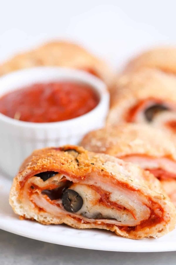 Close-up of a sliced stromboli filled with cheese, black olives, and pepperoni, served on a plate with a small bowl of marinara sauce in the background.