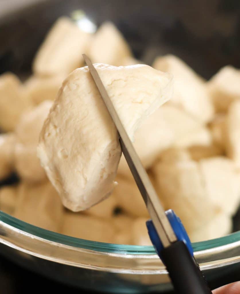 Cutting biscuits with scissors into a glass mixing bowl.