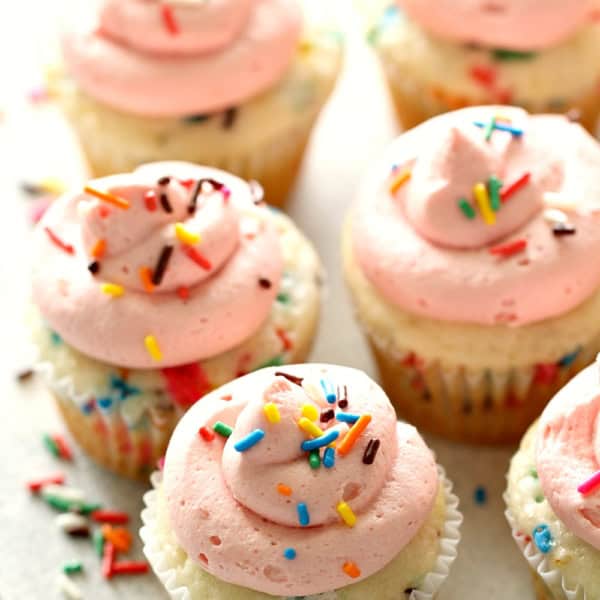 Confetti Cupcakes with Homemade Strawberry Buttercream Frosting on a white background with sprinkles spread around.