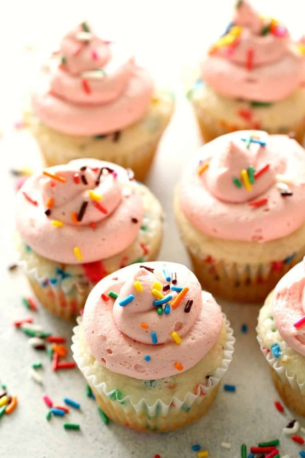 Confetti Cupcakes with Homemade Strawberry Buttercream Frosting on a white background with sprinkles spread around.
