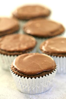 Chocolate cupcakes in silver wrappers with smooth, shiny frosting arranged in a group.
