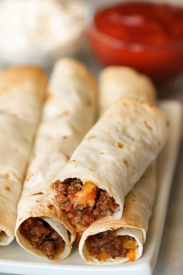 Baked Beef Taquitos stacked and served on a white serving plate
