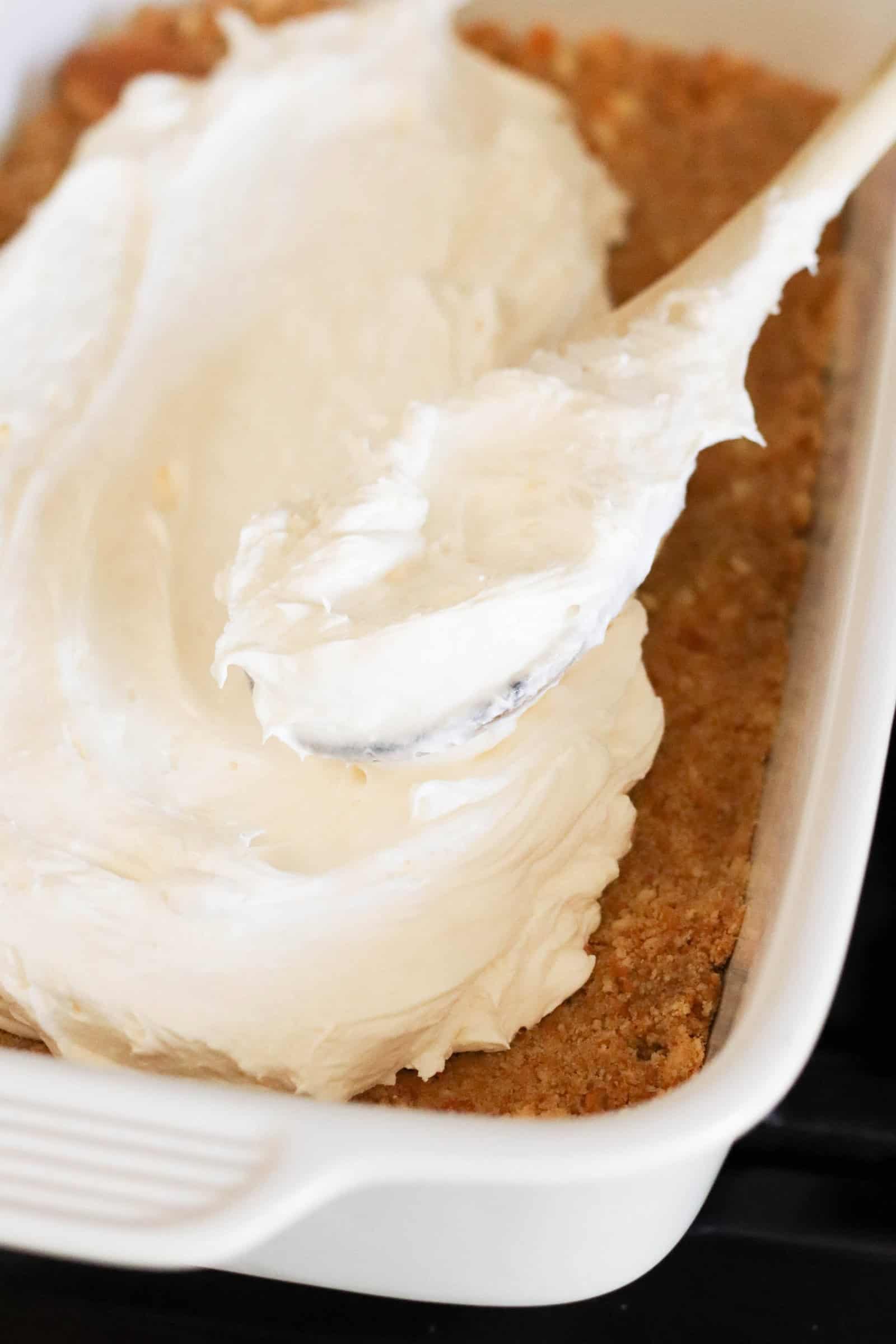 spreading the cool whip layer on top of the crust with a wooden spoon