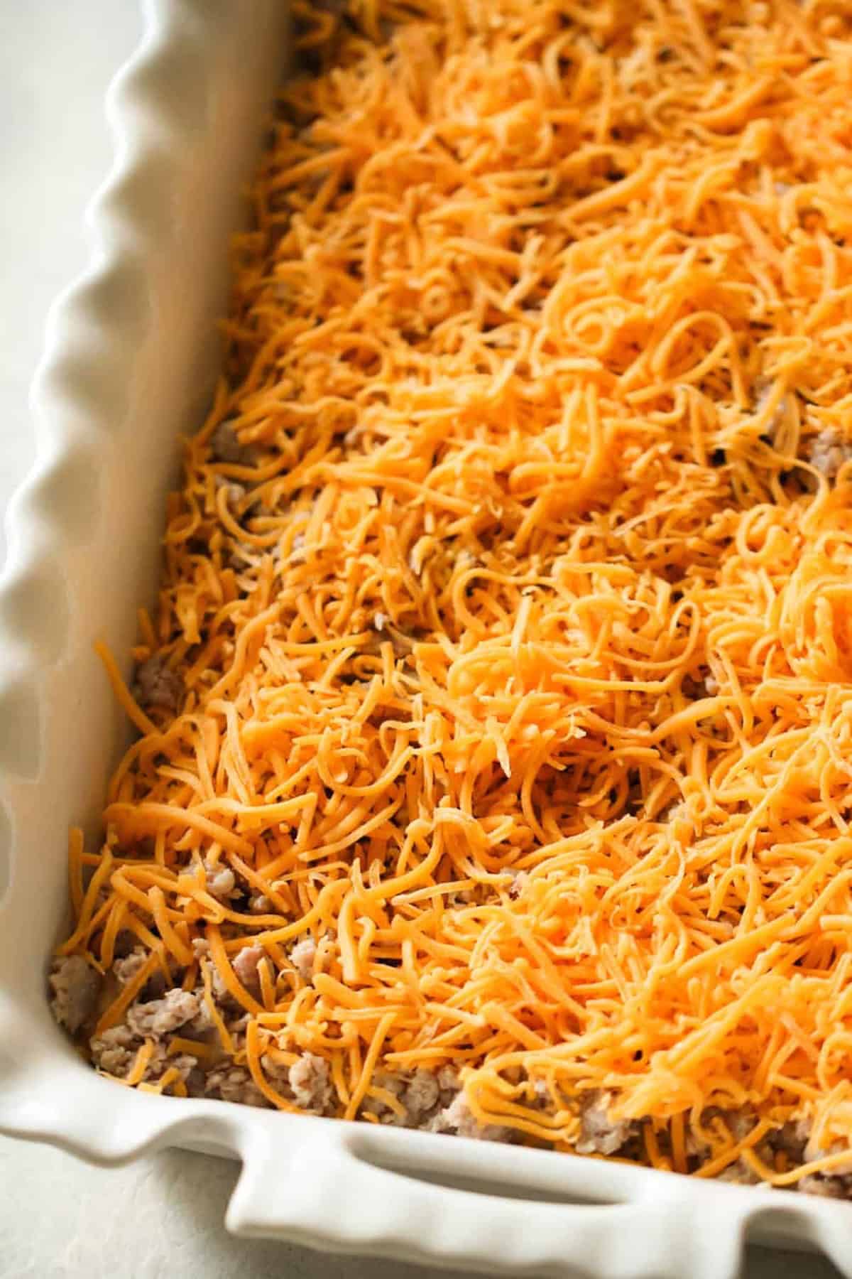 Shredded cheddar cheese layered over a mixture in a rectangular ceramic baking dish.