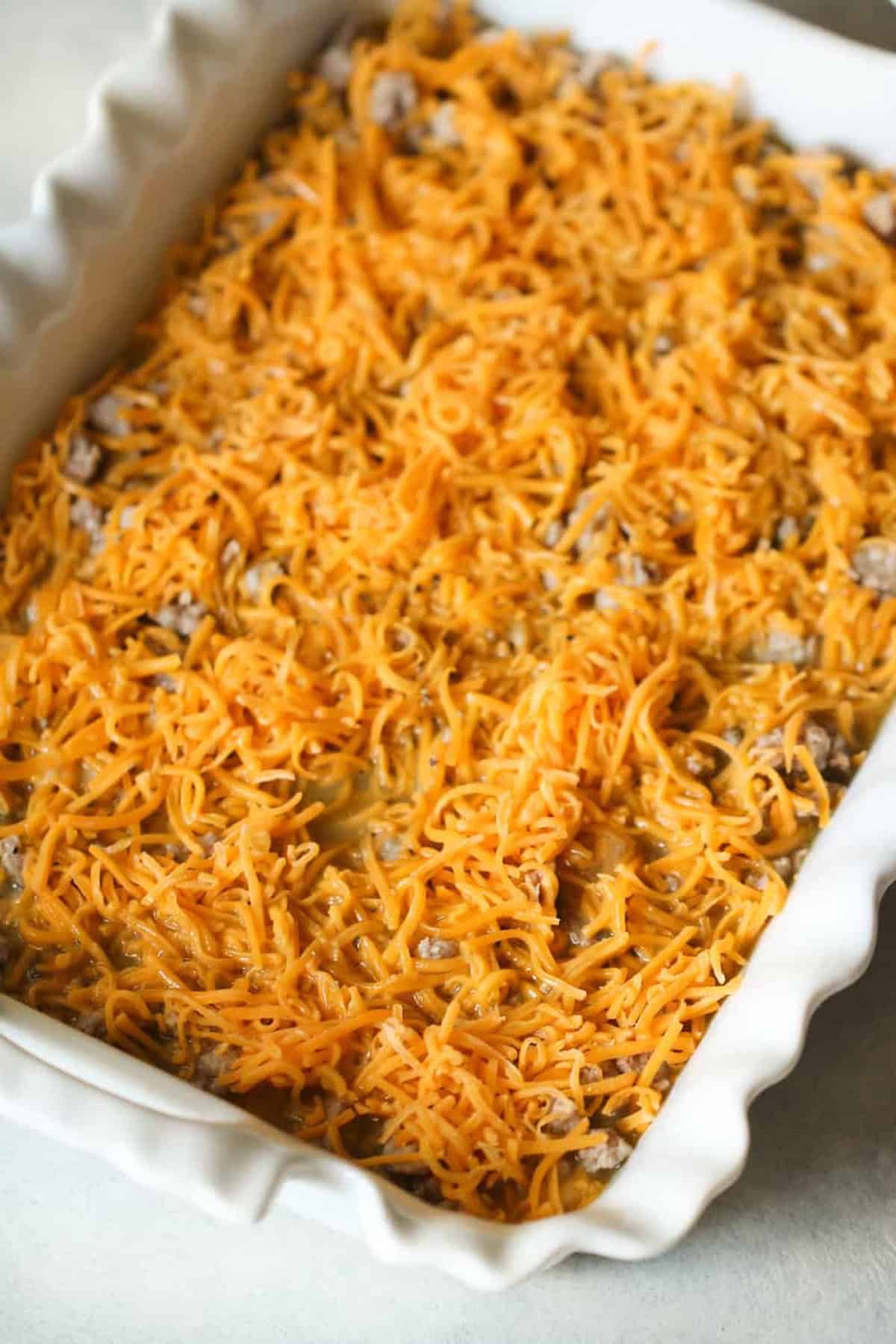 A rectangular baking dish filled with a casserole topped with shredded cheddar cheese and ground meat.