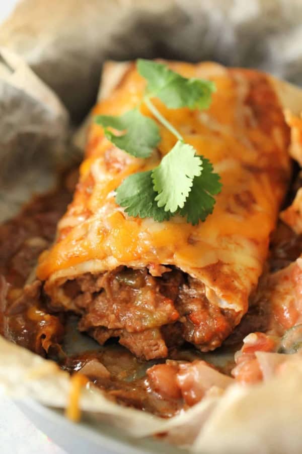 Close-up of a beef burrito with melted cheese and cilantro garnish.