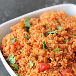 A bowl of Mexican rice garnished with chopped cilantro, featuring visible pieces of tomato and green pepper, served on a dark countertop.