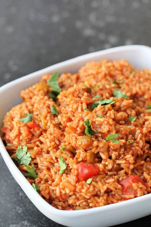 A bowl of Mexican rice garnished with chopped cilantro, featuring visible pieces of tomato and green pepper, served on a dark countertop.