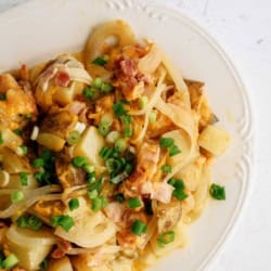 A plate of diced potatoes mixed with cooked onions, chopped bacon, melted cheese, and topped with sliced green onions.