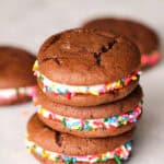 A stack of three chocolate whoopie pies with colorful sprinkles and a cream filling are arranged on a white surface.