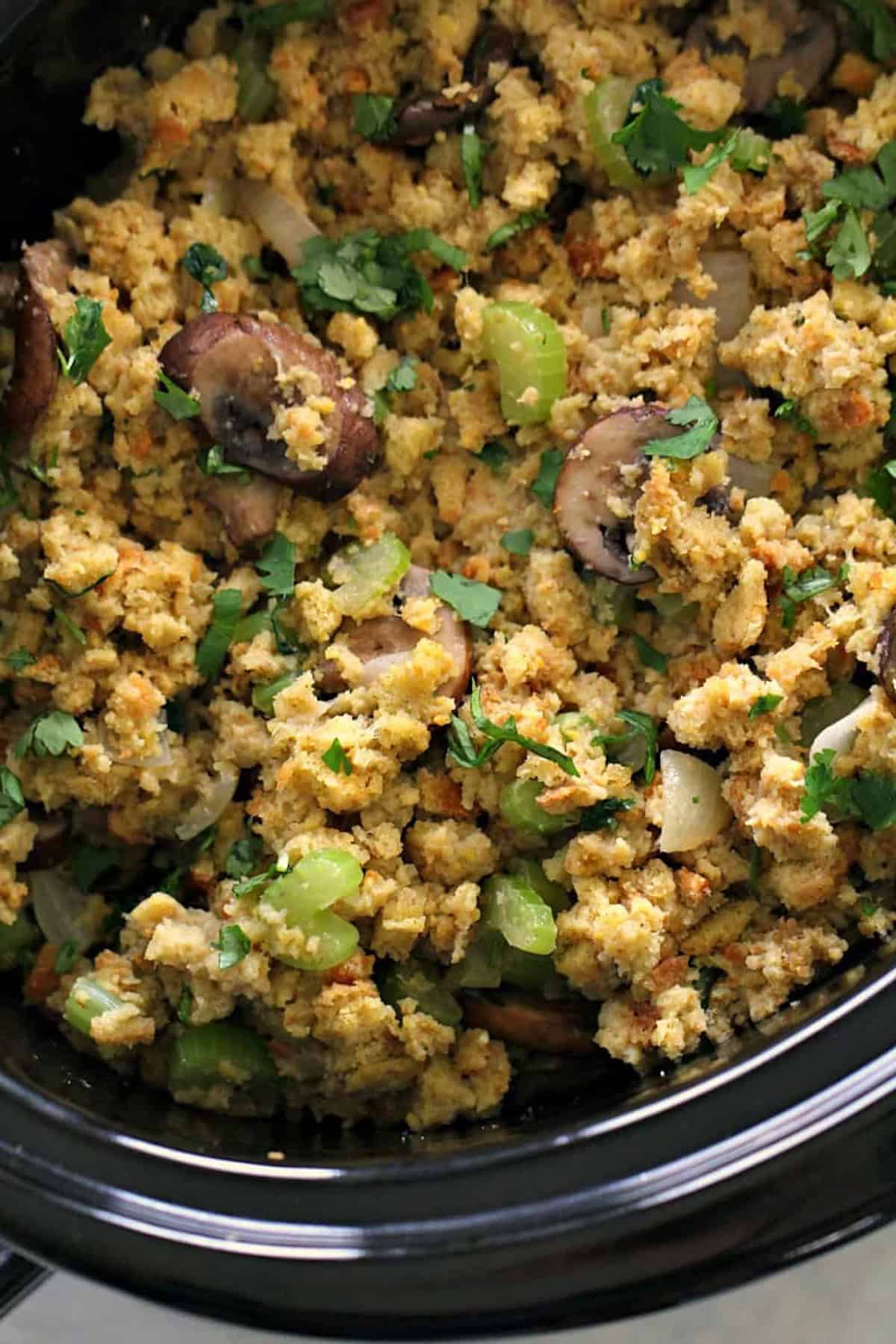 Slow cooker filled with cornbread stuffing mixed with celery, mushrooms, onions, and fresh herbs.