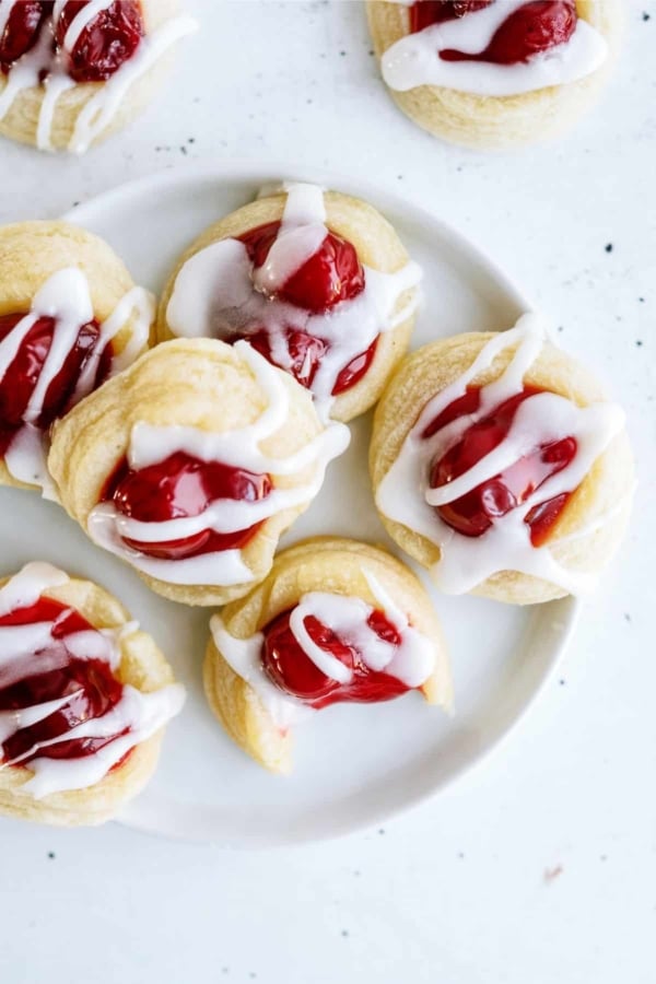 A plate of six cherry Danish pastry cookies drizzled with white icing.