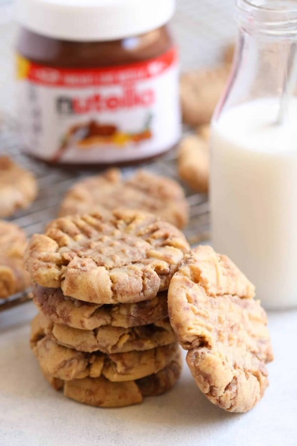 A stack of Peanut Butter Nutella Swirl Cookies with a jar of nutella in the background and a glass of milk off to the side.