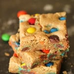 3 Thick and Chewy M&M Blondies stacked on top of each other surrounded by M&M's.