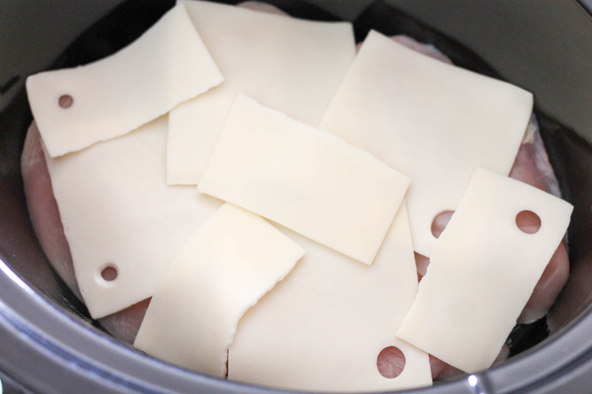 Slices of swiss cheese covering raw chicken in slow cooker