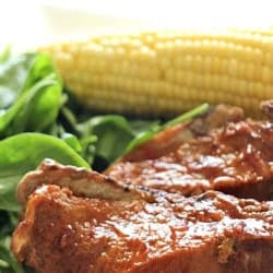 A plate with a slow cooker pork chop, a serving of leafy greens and corn.