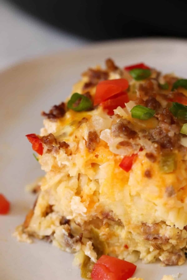Close-up of a slice of breakfast casserole with eggs, sausage, cheese, and diced green onions and tomatoes on a plate.