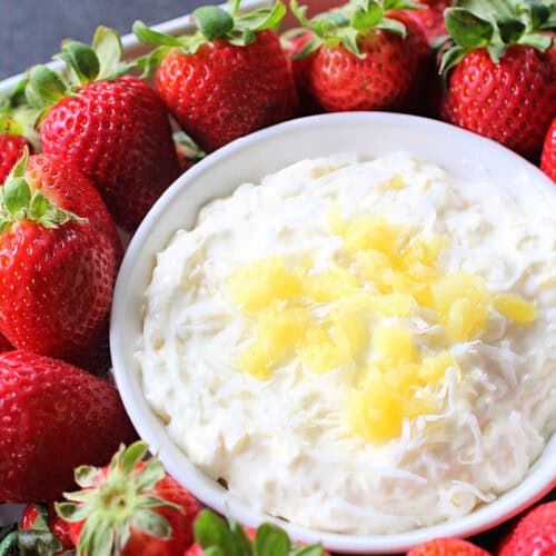 A bowl of Piña Colada Fruit Dip surrounded by fresh strawberries.