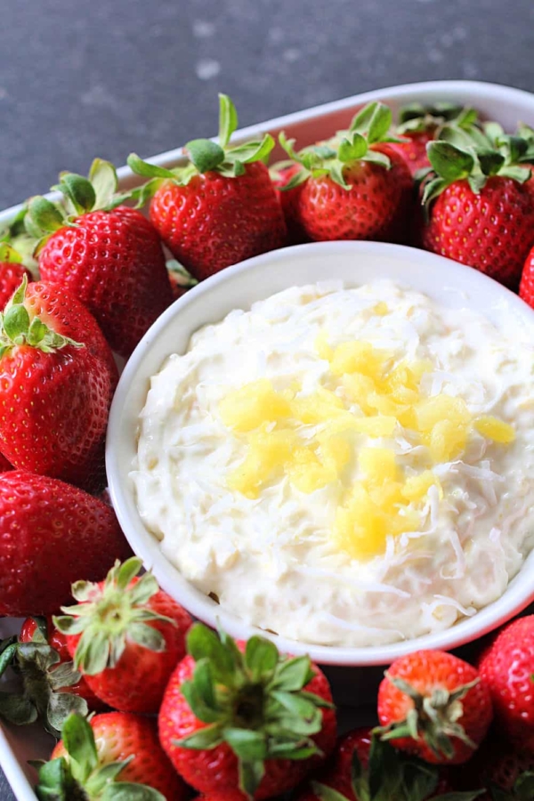 A bowl of Piña Colada Fruit Dip surrounded by fresh strawberries.