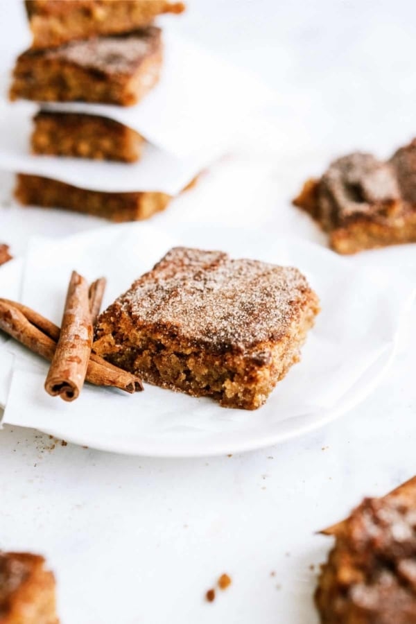 One Snickerdoodle Blondie on a plate with a cinnamon stick. Other Snickerdoodle Blondies on plates in the background.