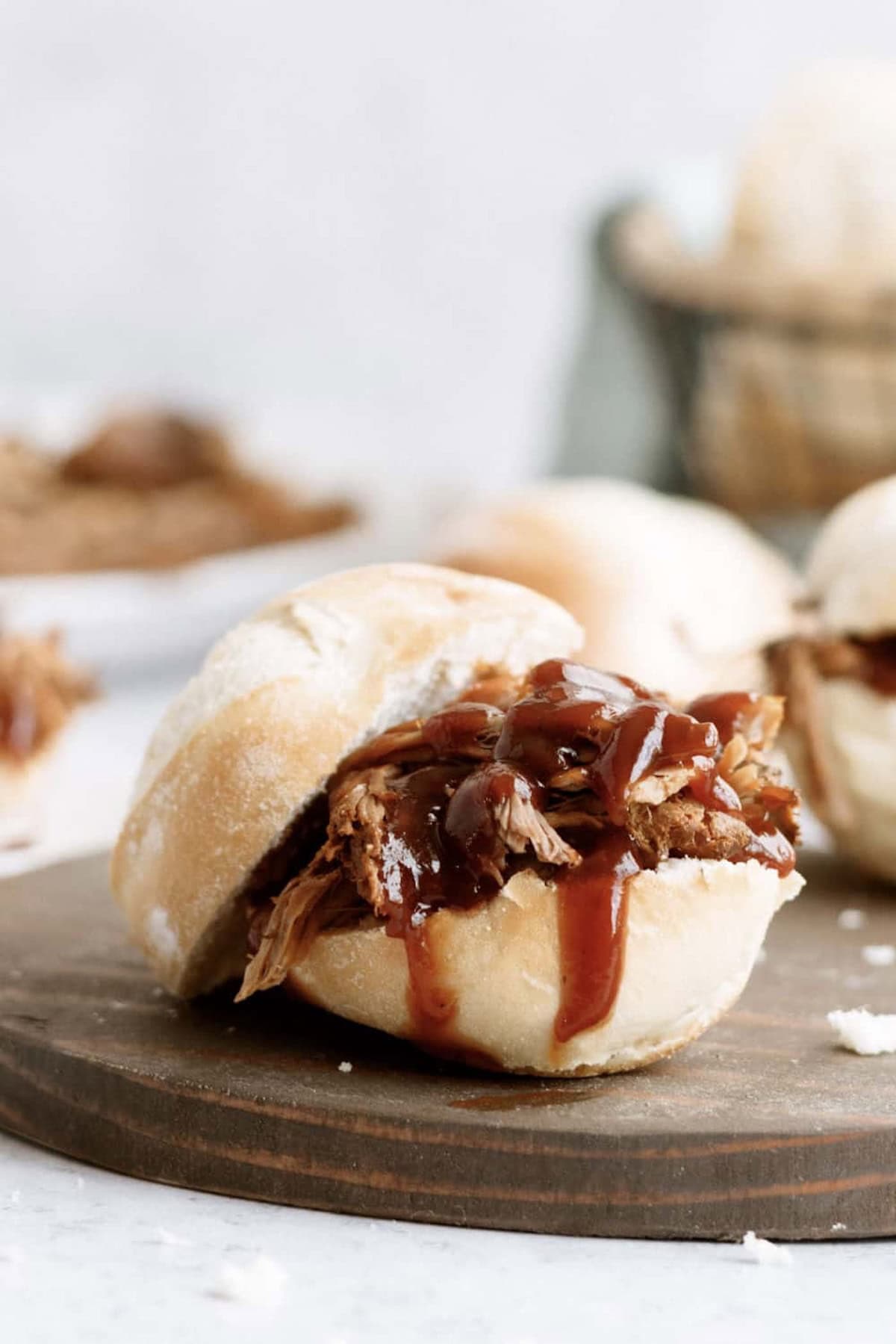 Pulled pork sandwich with barbecue sauce on a round bread roll, resting on a wooden board.