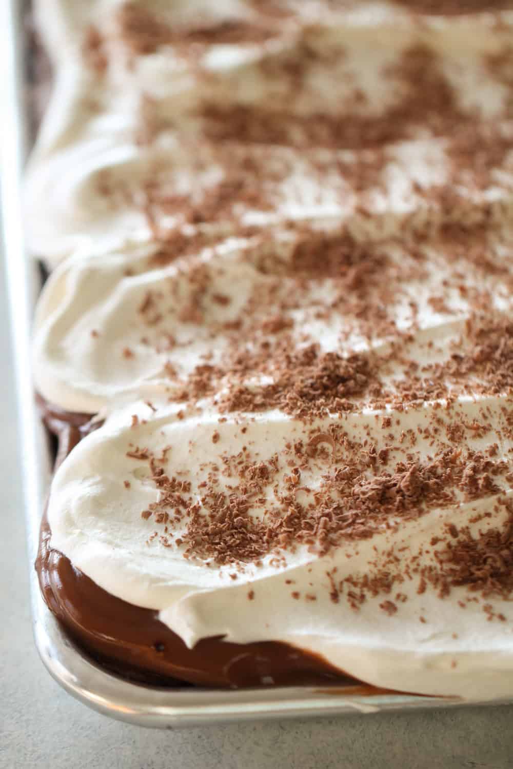 Chocolate Pudding Cake in a sheet pan topped with cool whip and chocolate shavings.