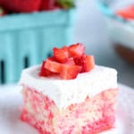 A slice of Strawberries and Cream Poke Cake on a plate topped with fresh strawberries.