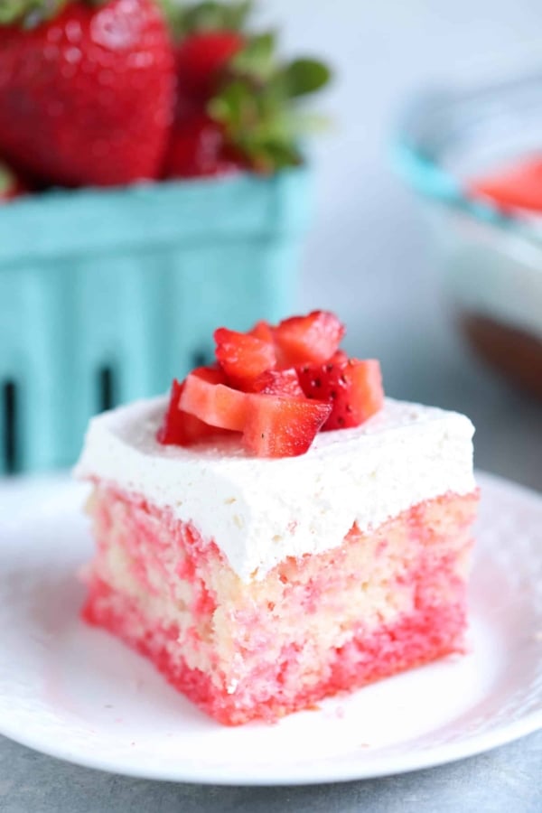 A slice of Strawberries and Cream Poke Cake on a plate topped with fresh strawberries.