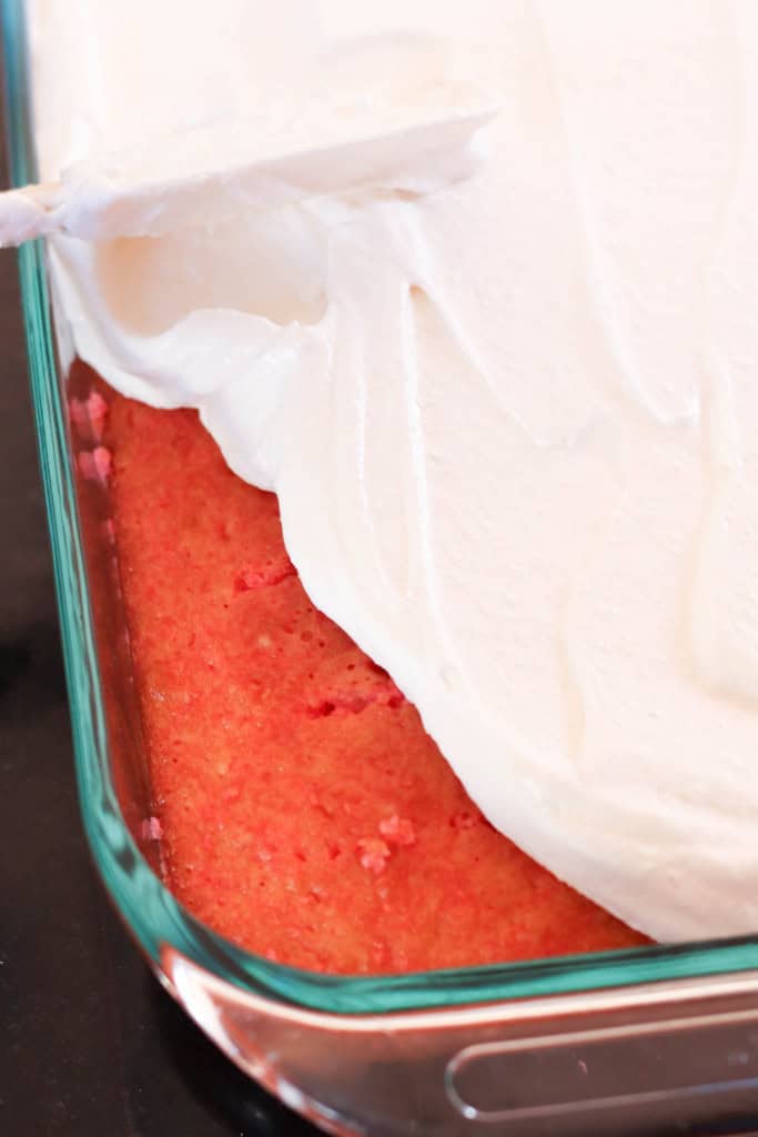 Frosting spread over Strawberries and Cream Poke Cake.