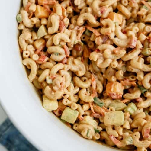 Close-up of a bowl of macaroni salad with elbow noodles, diced vegetables, and a creamy dressing, served in a white dish.