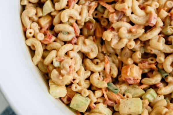 Close-up of a bowl of macaroni salad with elbow noodles, diced vegetables, and a creamy dressing, served in a white dish.