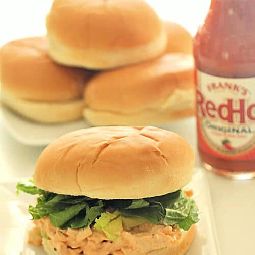 Buffalo Chicken Salad Sandwiches on plate with a bottle of buffalo sauce.