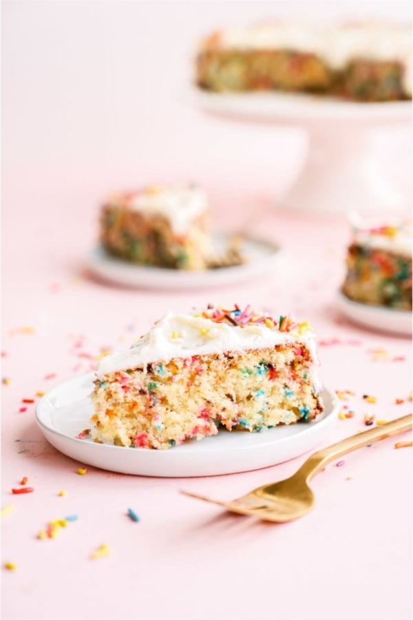 A slice of Funfetti Cake and Buttercream Frosting on a plate with other plates with slices of cake in background,
