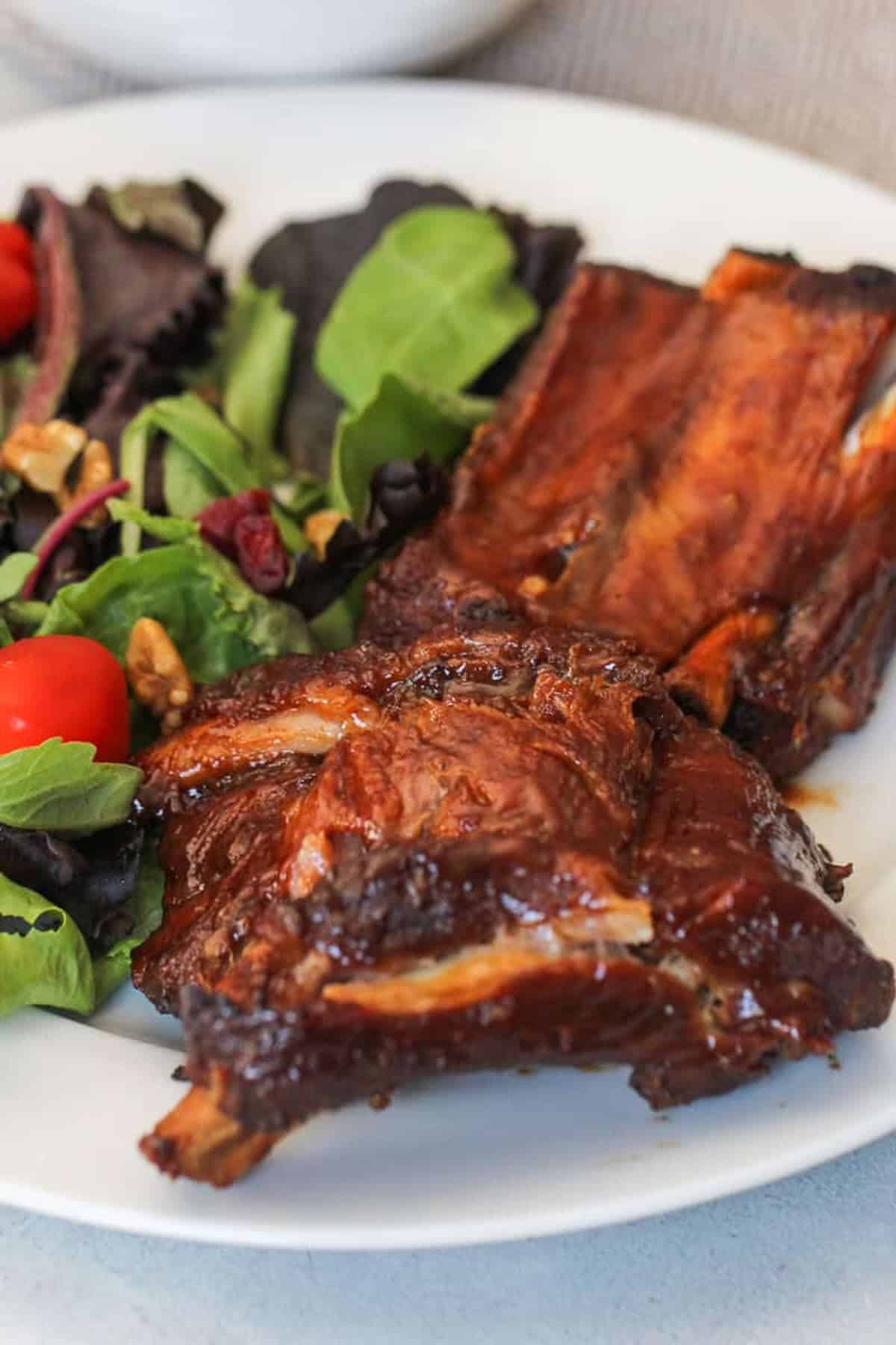Plate with barbeque glazed ribs and a mixed green salad with cherry tomatoes and walnuts.