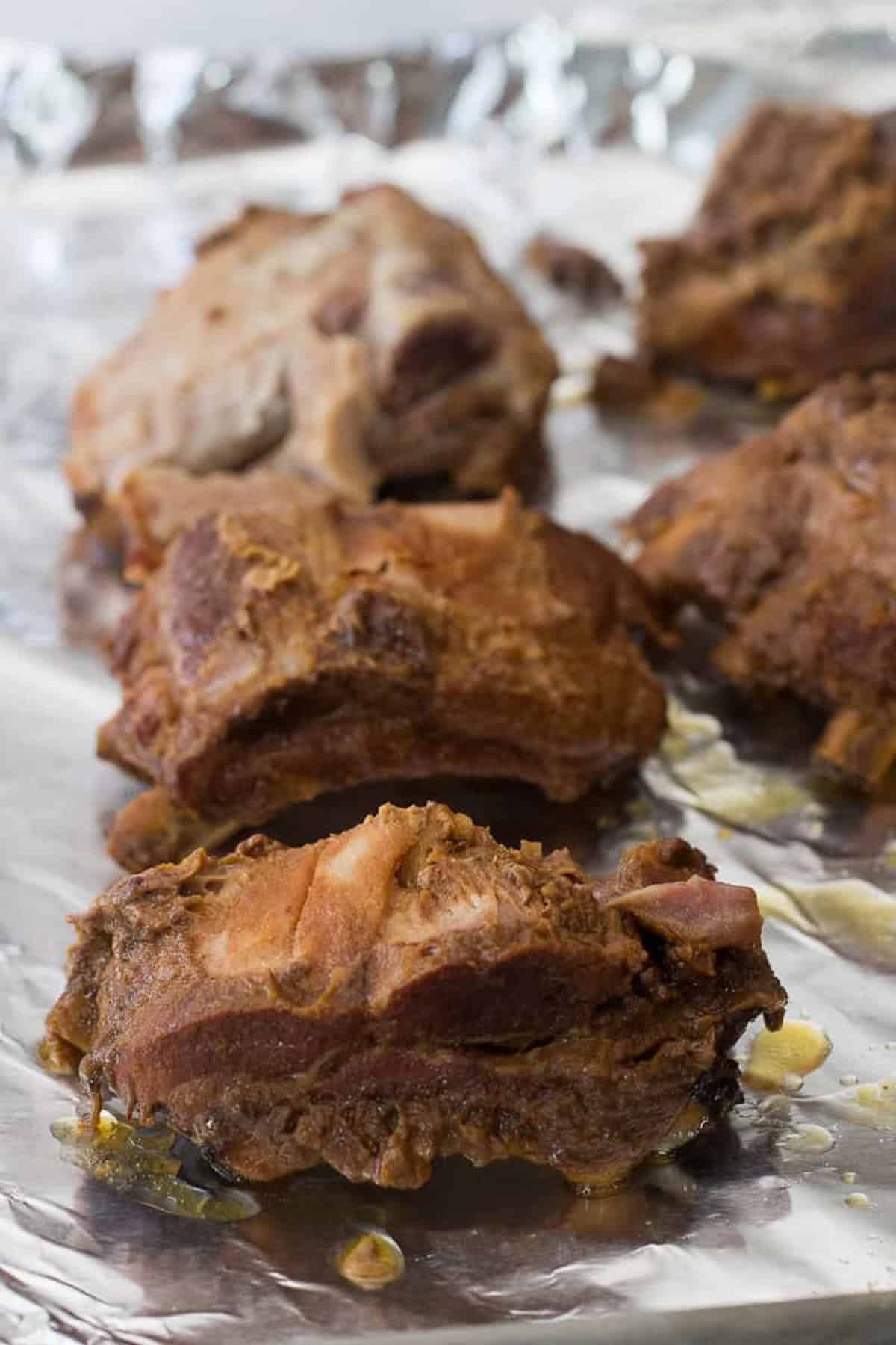 Close-up of cooked pork ribs resting on a sheet of aluminum foil.